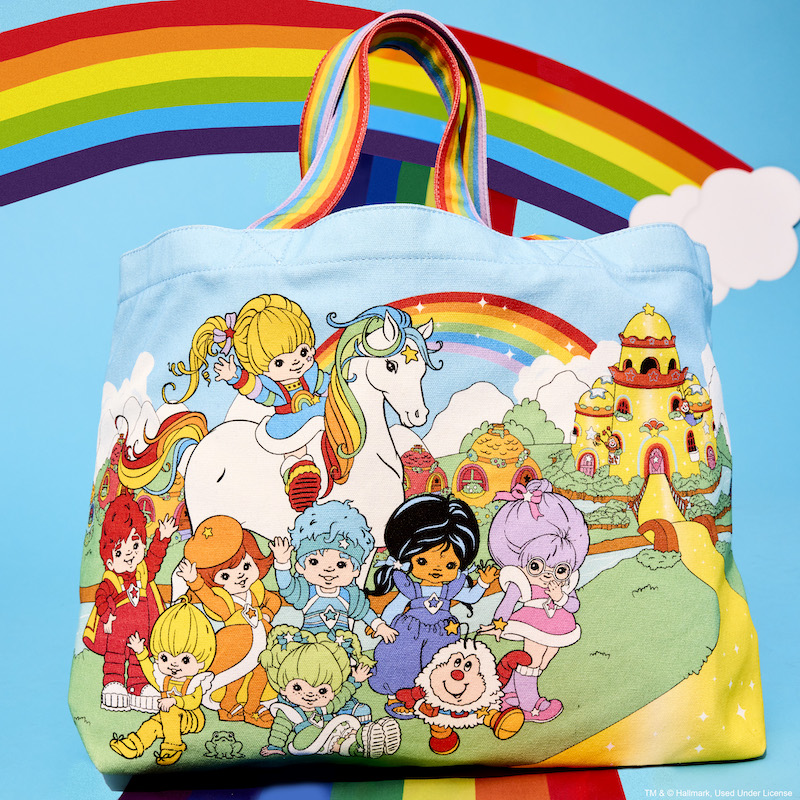 Loungefly Rainbow Brite The Color Kids Canvas Tote Bag featuring the Color Kids and a rainbow handle sitting on a rainbow against a blue background